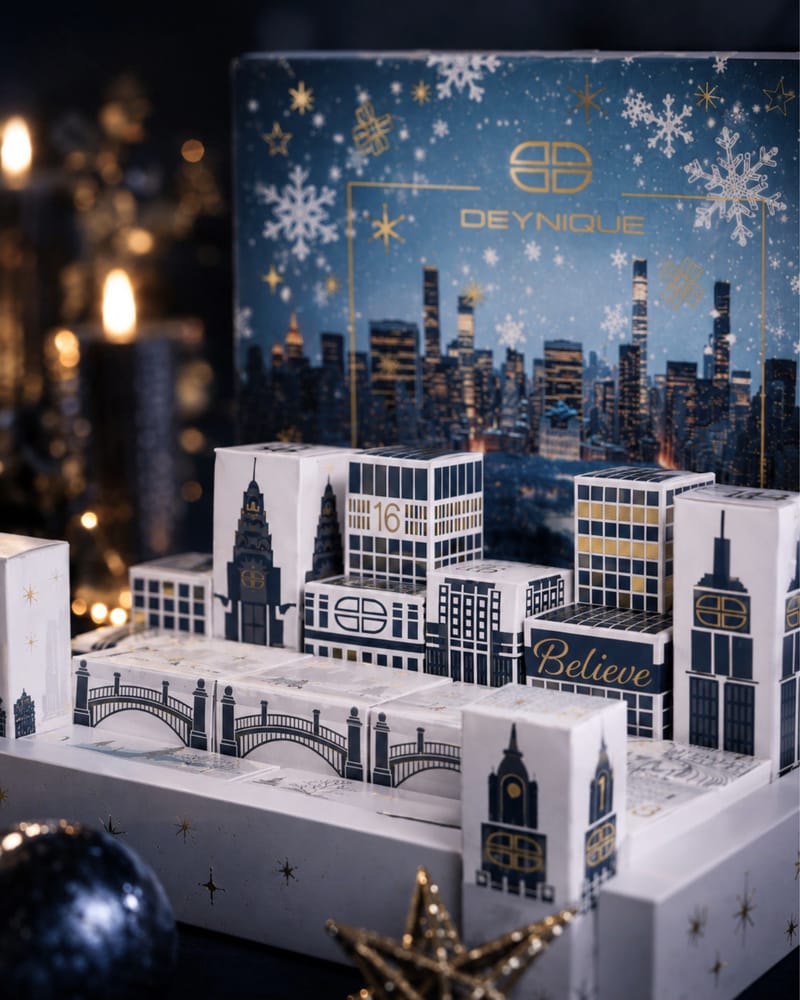 Die Türchen des DEYNIQUE Adventskalenders 2026 im Kerzenlicht, als kleine New Yorker Stadtkulisse aufgestellt