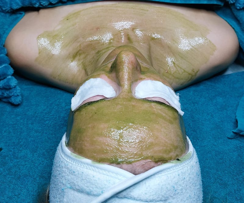 Grüne Detox-Maske auf Gesicht und Dekolleté in der Kabine