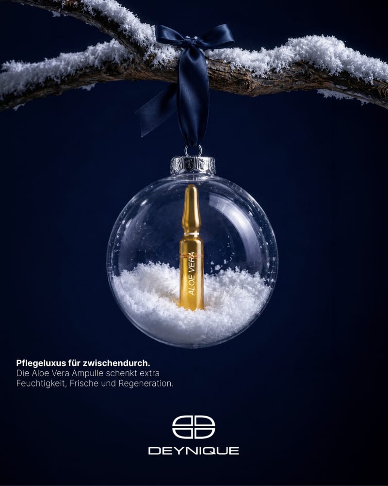 DEYNIQUE Aloe Vera Ampulle in einer Christbaumkugel mit Schnee an einem verschneiten Ast. Bildtext: Pflegeluxus für zwischendurch. Die Aloe Vera Ampulle schenkt extra Feuchtigkeit, Frische und Regeneration.
